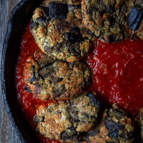 close-up overhead of eggplant patties in sauce in a cast iron skillet.