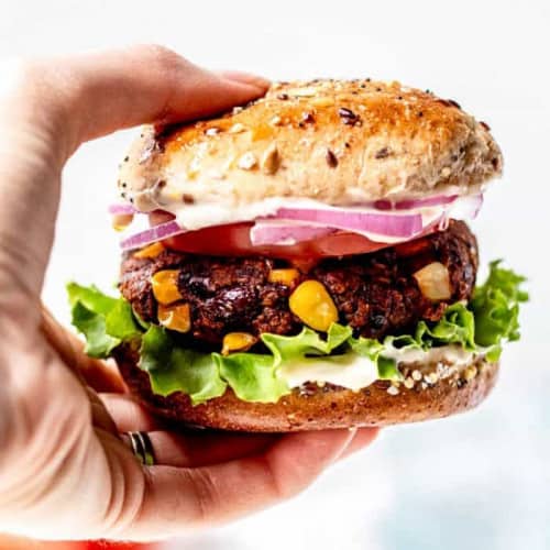 holding up a black bean burger with toppings and a bun.