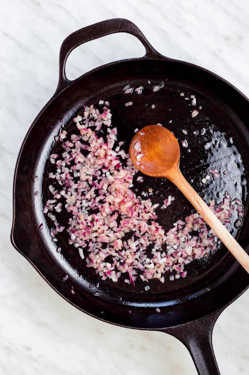 Sautéing diced red onion in a black cast iron skillet with a wooden spoon in it.