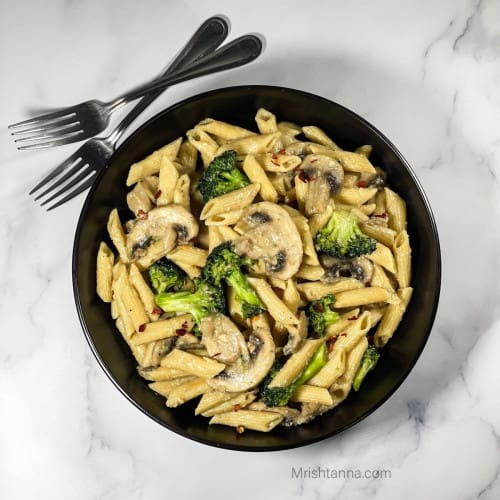 overhead of mushroom and broccoli pasta in a black bowl with two forks behind it.