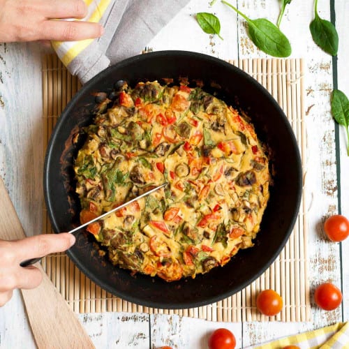 Hands cutting into a vegan frittata in a pan.
