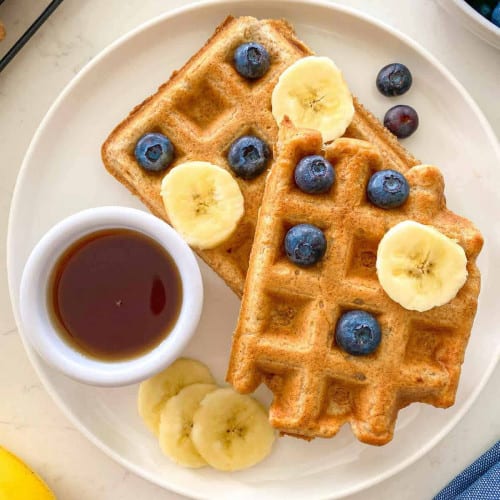 Waffles on a plate with syrup, blueberries and banana.