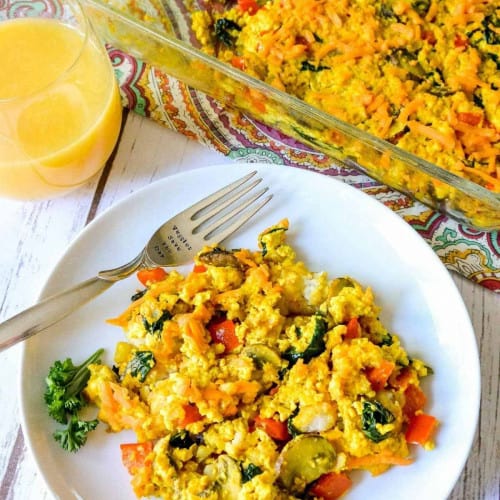 Vegan egg casserole on a plate with a fork to the side and the casserole dish in the back.