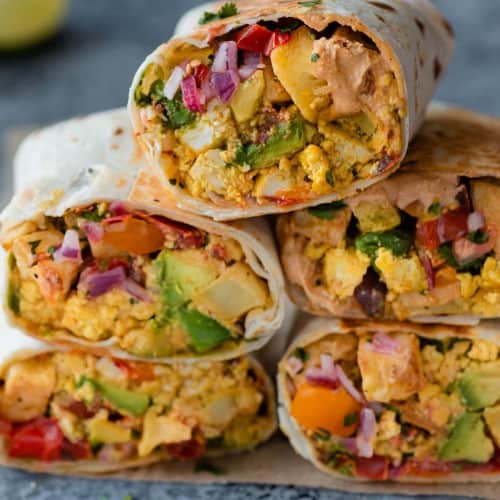 Vegan breakfast burritos stacked up on a plate.