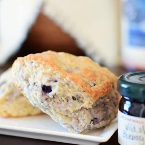 Vegan scones on a plate with a jar of jam to the side.