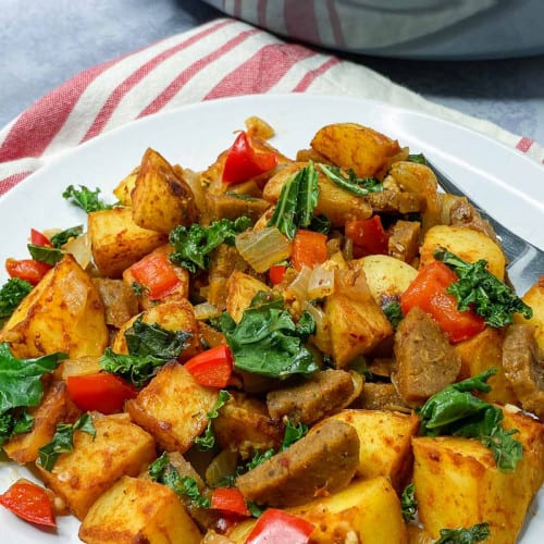 Breakfast potatoes on a plate with peppers and spinach.