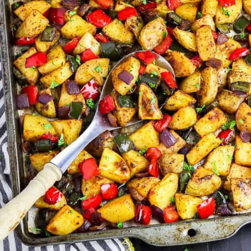 Potatoes and veggies on a sheet pan with a spoon at an angle with some potatoes in it.