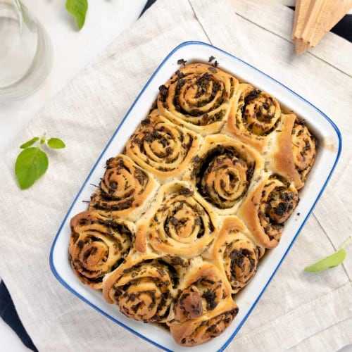 Oregano rolls in a baking dish with fresh herb leaves around them.