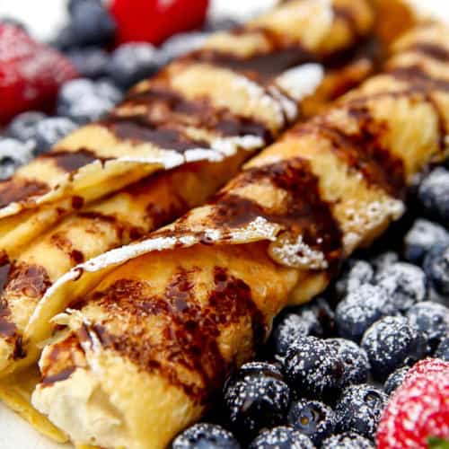 Plate of crepes dusted with powdered sugar and served with berries.