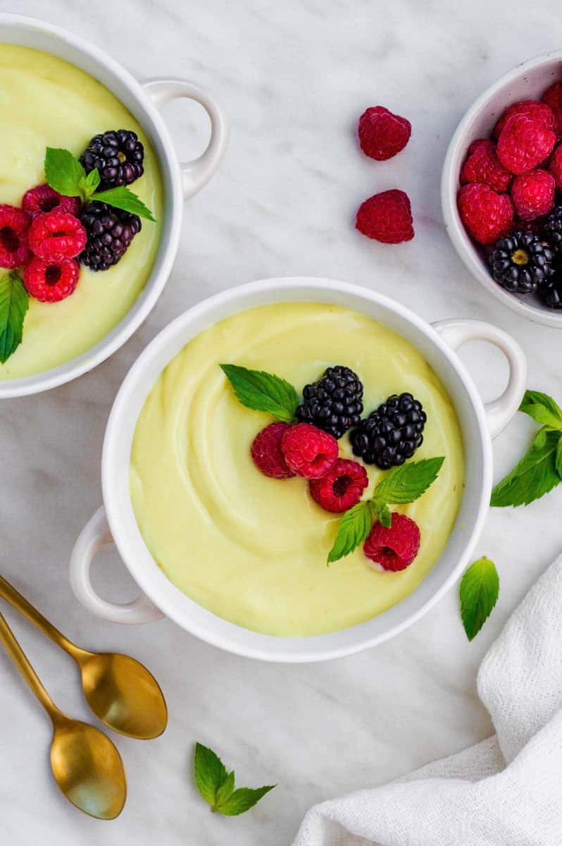 A small white bowl filled with my vegan vanilla custard recipe and topped with raspberries, blackberries and fresh mint leaves.