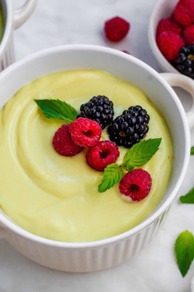 A close-up shot of vanilla custard served in a white bowl and topped with berries and mint leaves.