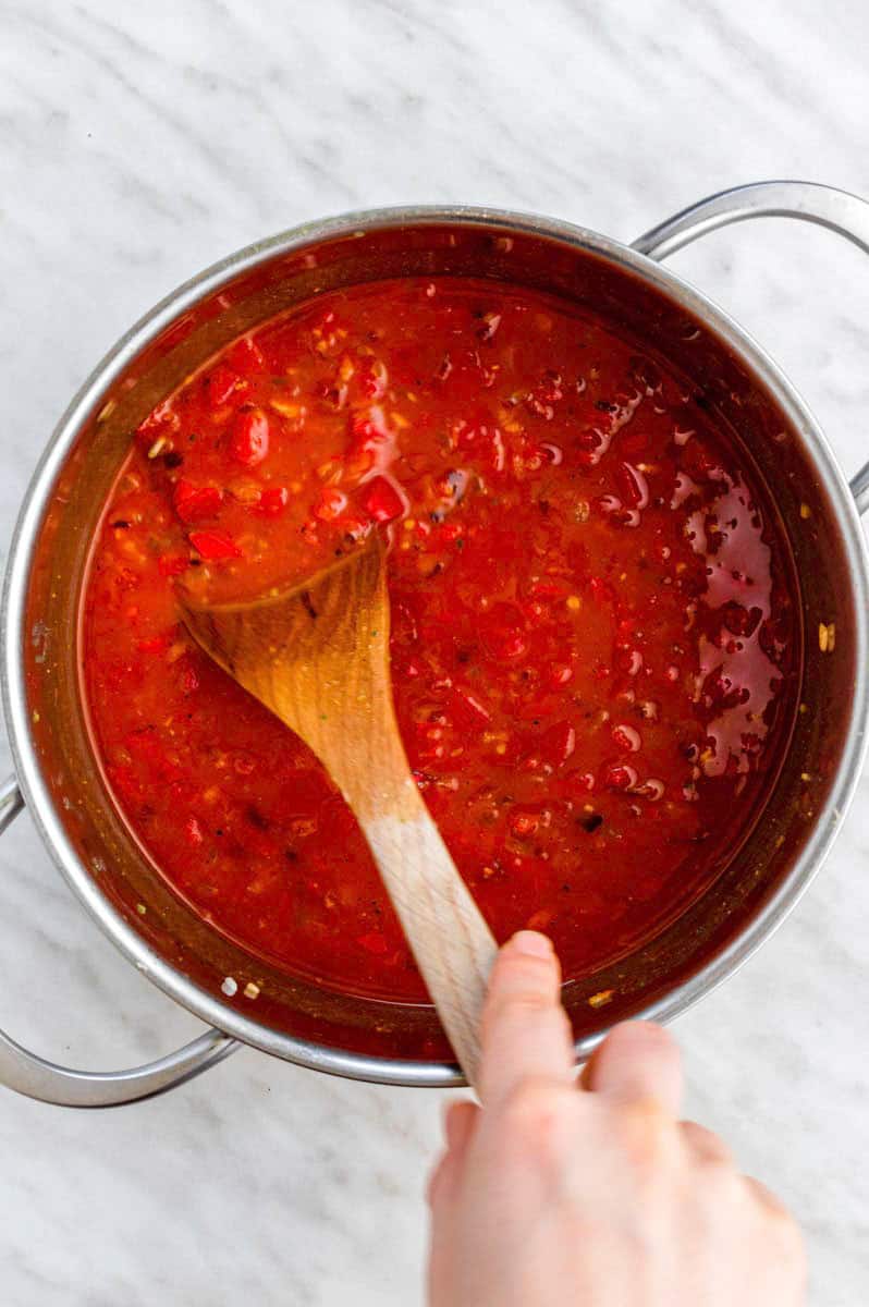 Stirring tomato sauce with a wooden spoon from a stainless-steel pot.