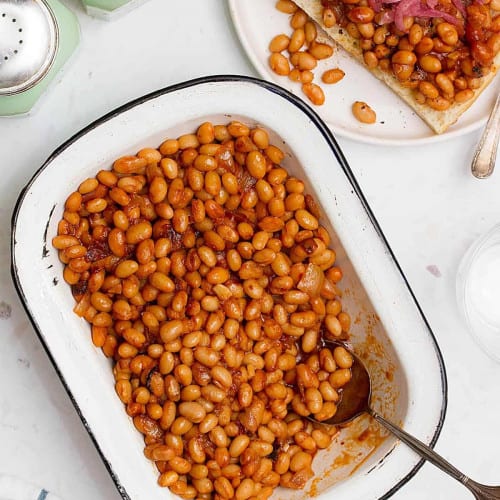 Baked beans in a rectangle white casserole dish with a spoon.