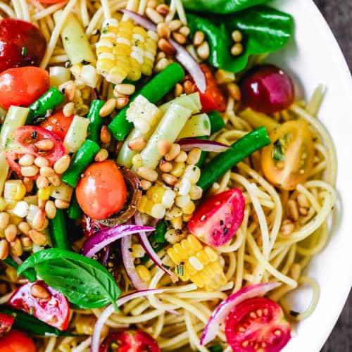 Bowl of spaghetti salad with lots of colorful fresh vegetables.