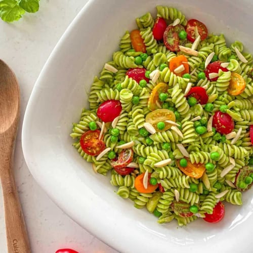 Pesto pasta salad in a bowl with tomatoes and sliced almonds.
