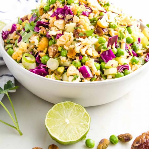 Colorful salad with peas and cabbage on the table and pistachios around on the table.