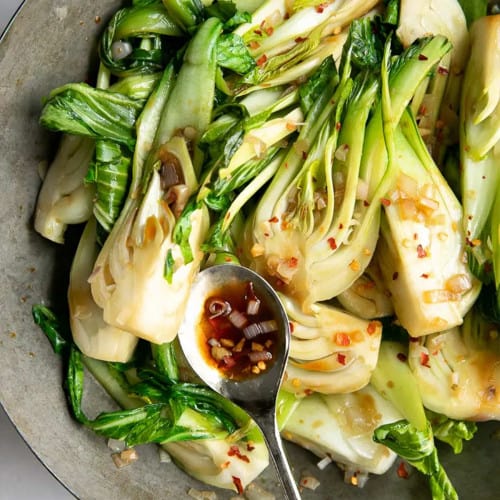 Sauteed bok choy in a wok with a spoon holding a little bit of sauce the veggie is cooked with.