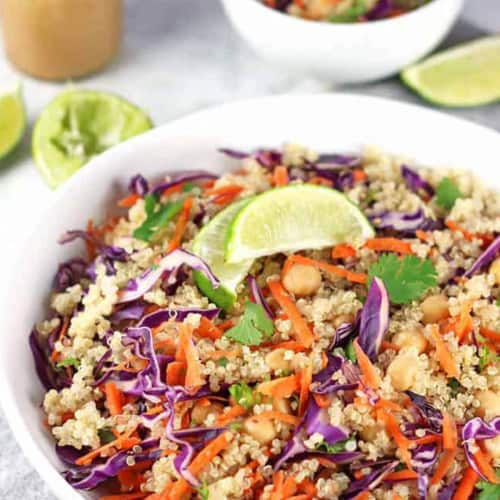 Colorful quinoa salad in a white bowl garnished with lime wedges.