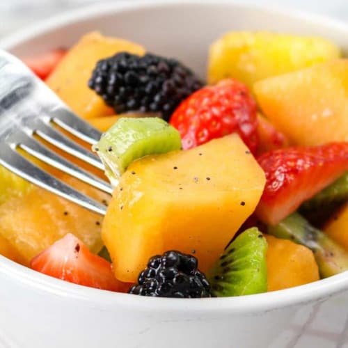 Fresh fruit salad in a bowl with a fork piercing a piece of fruit.