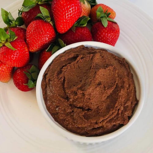 A bowl of chocolate hummus next to a pile of strawberries.