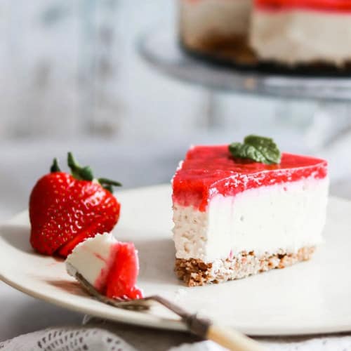 A bite of cheesecake on a fork on a plate with a slice and fresh strawberry.