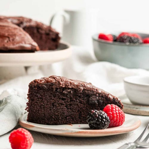 Chocolate cake with fresh berries on a plate with cake on a stand in the background.