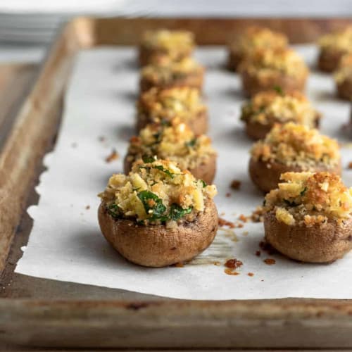 front view of stuffed mushrooms on parchment paper on a baking sheet.