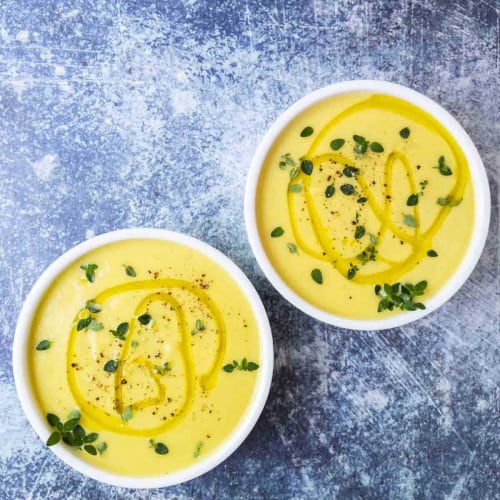 Two bowls of yellow squash soup on a blue background.