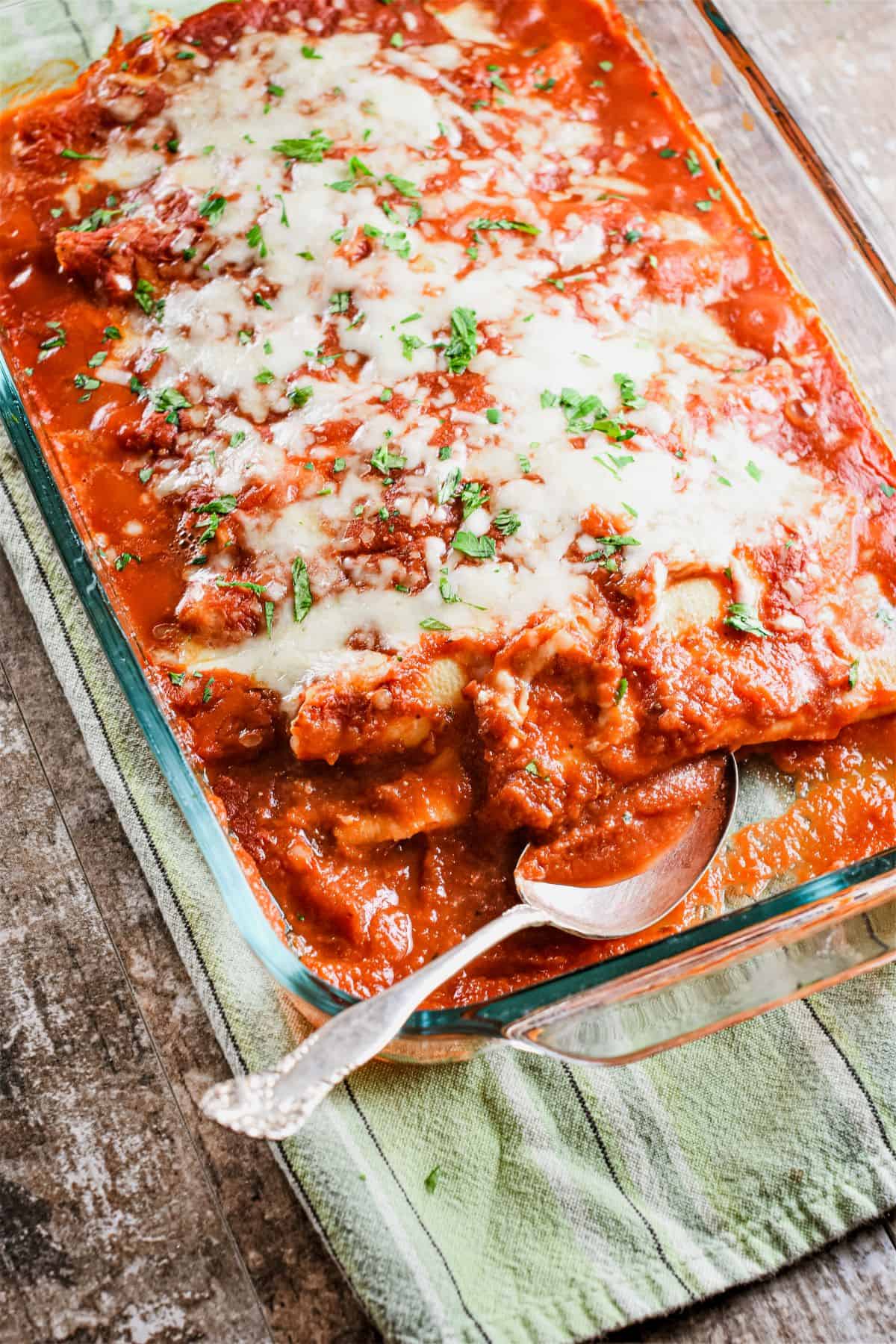 manicotti in baking dish with a spoon in it and some missing.