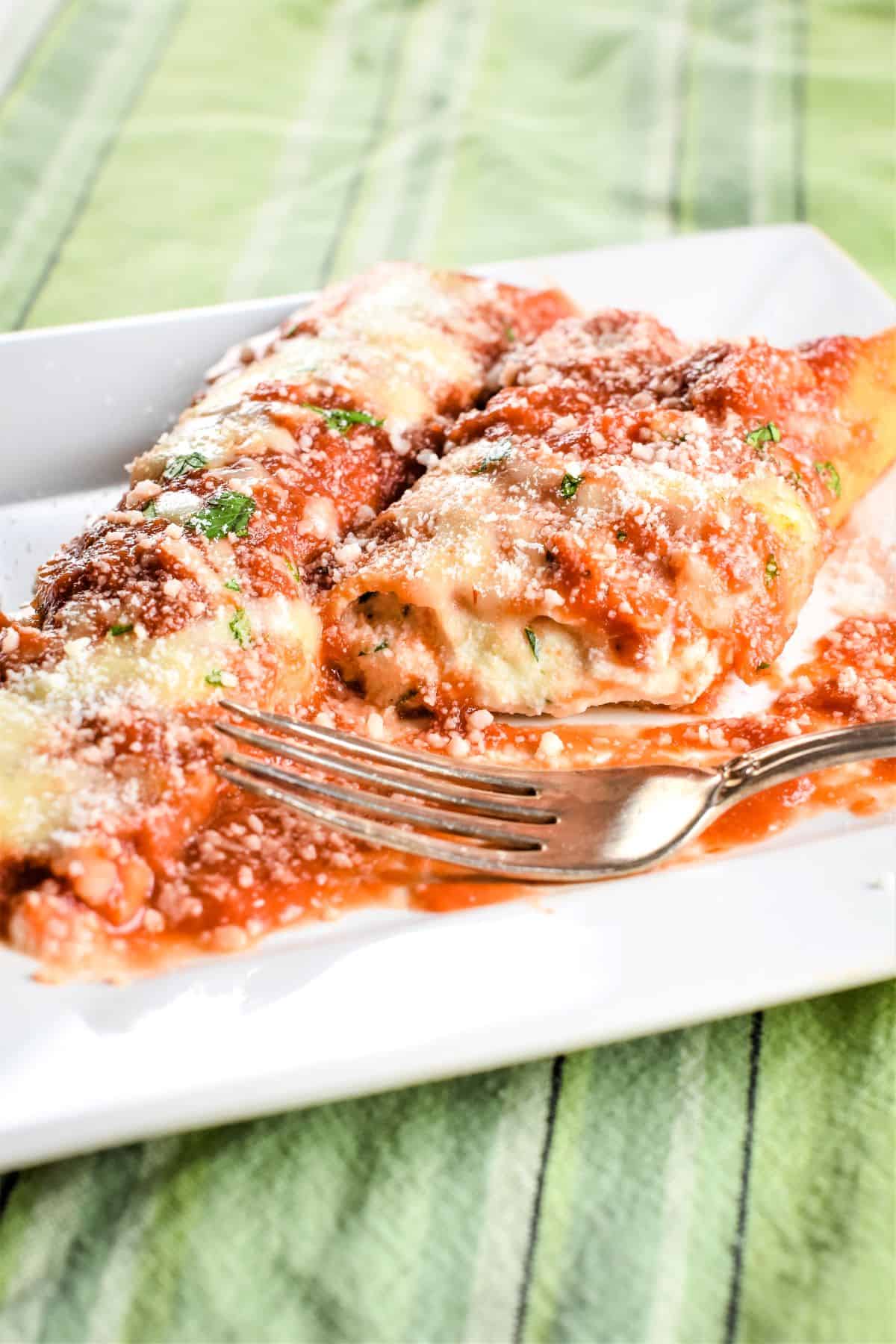 close-up of open manicotti on a white plate to expose the inside with a fork on the plate.