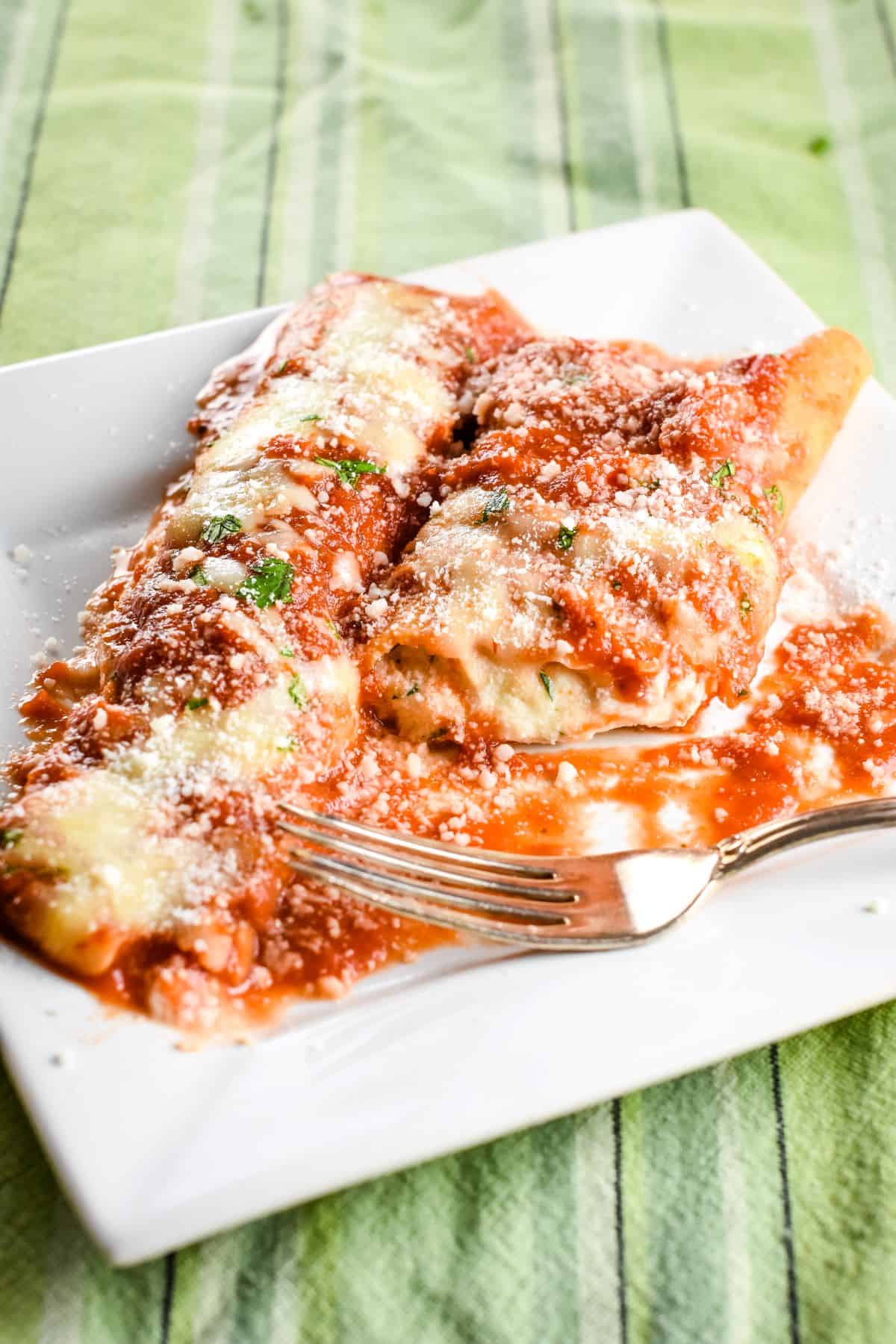 slight overhead of two manicotti in a white plate with one opened up.