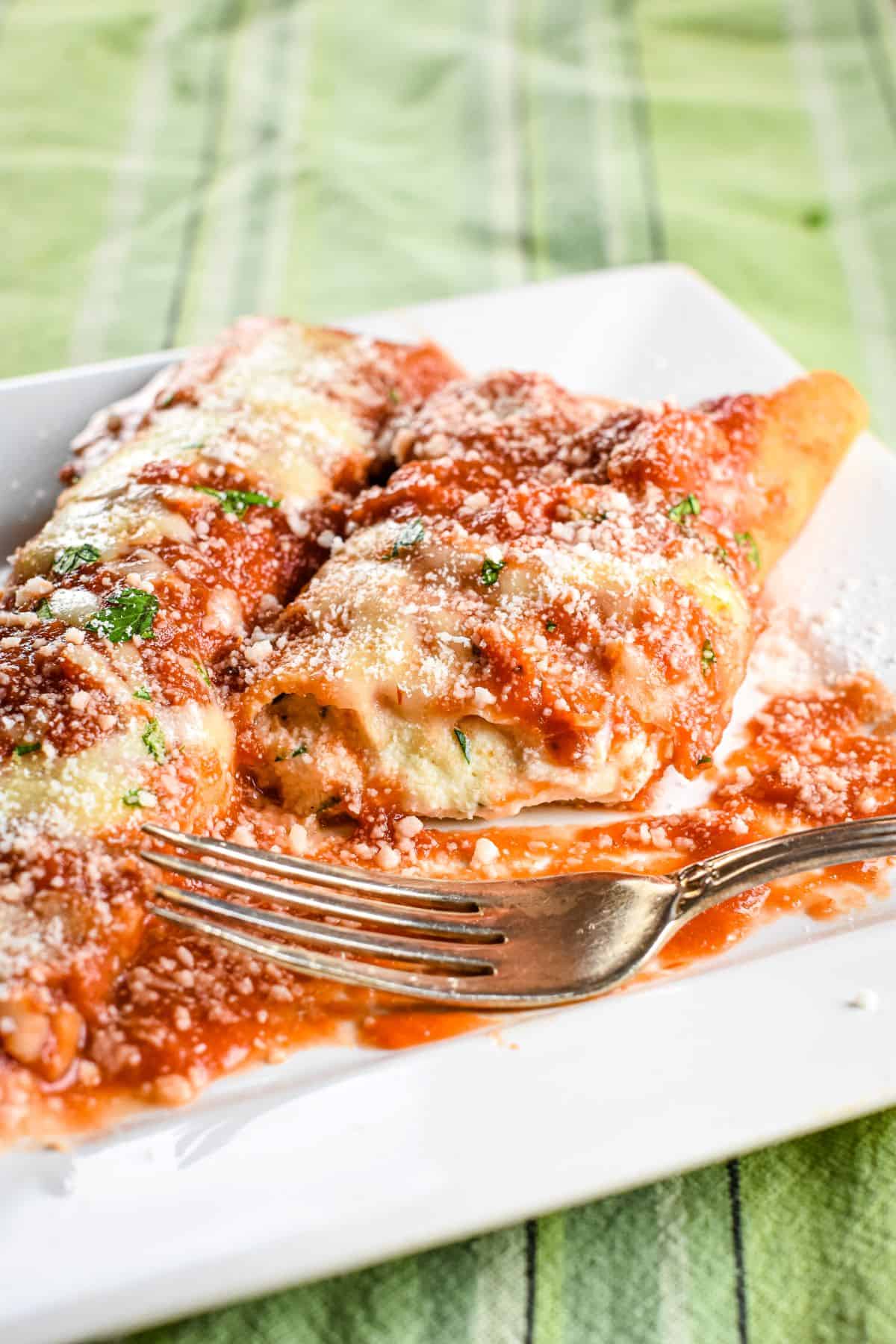 homemade manicotti on a white plate with a fork on it.