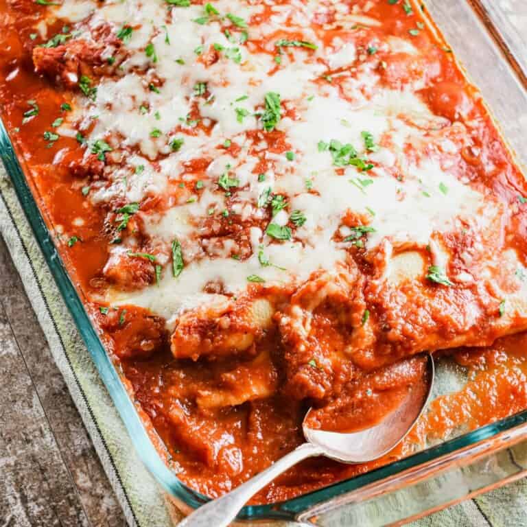 close-up of manicotti in baking dish with spoon in it and some taken out.