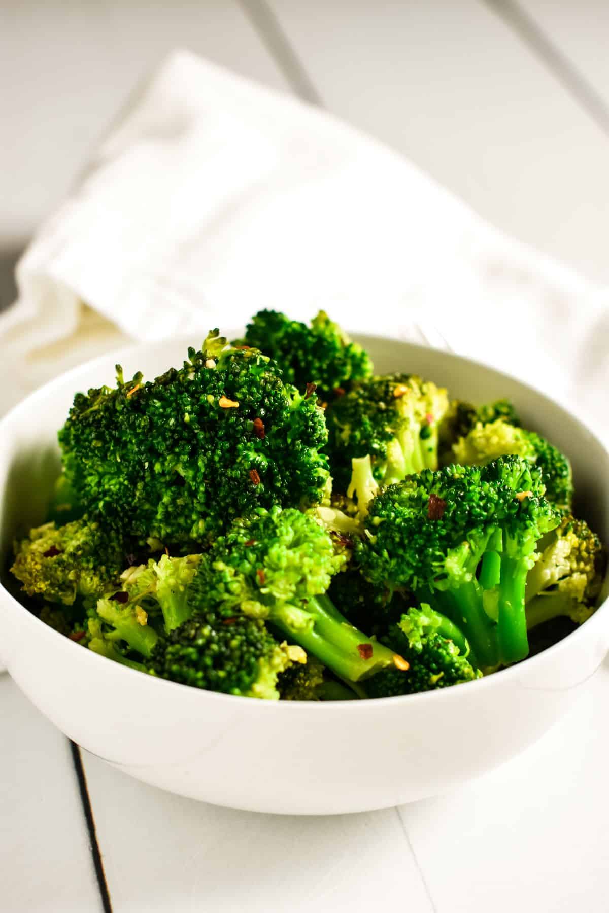 front view of cooked broccoli in a white bowl.
