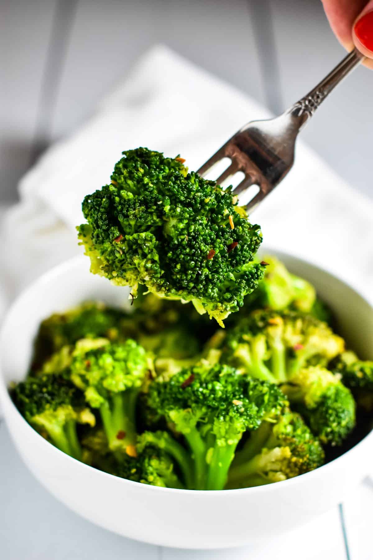 fork holding up a piece of broccoli over the bowl of the rest.