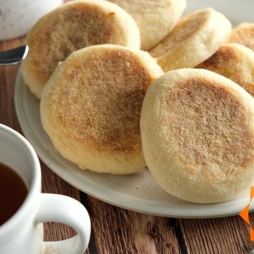 vegan English muffins on a white plate with cup of tea in the front.