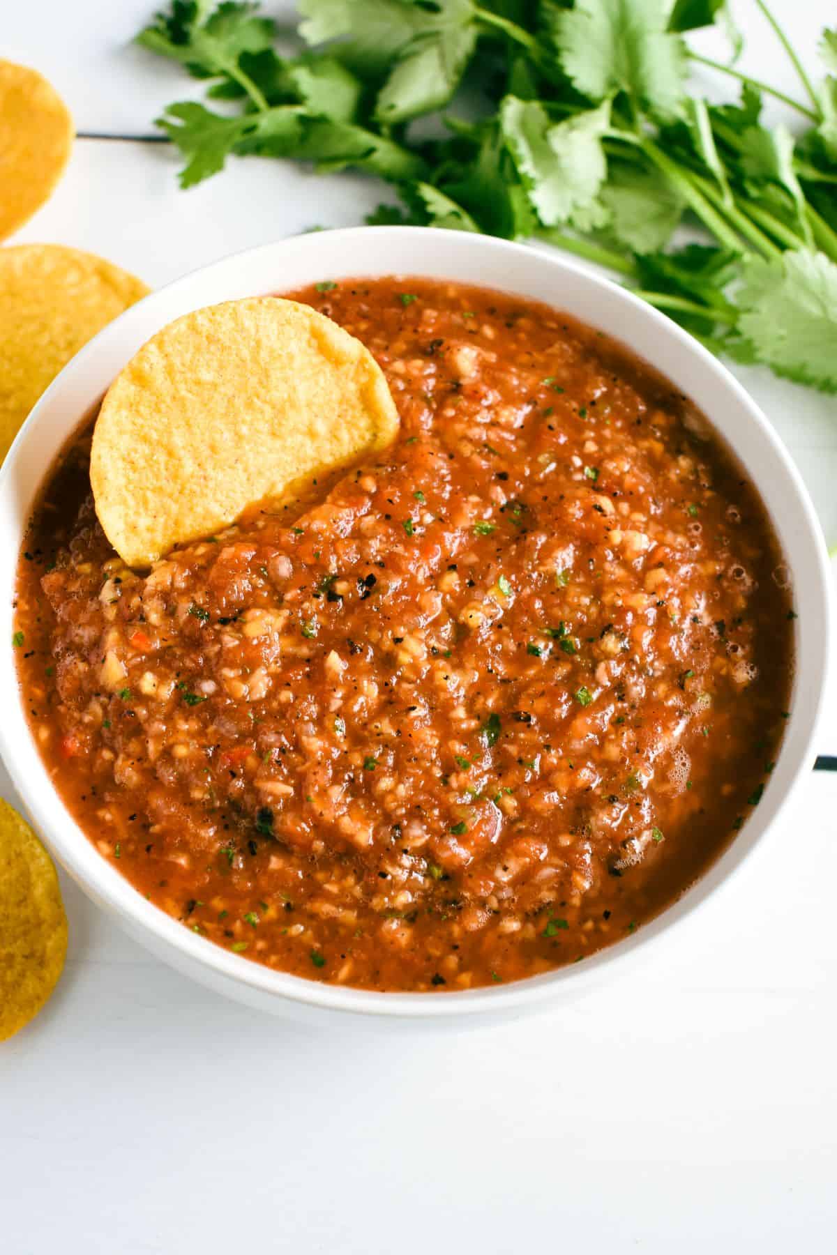 overhead of salsa in a white bowl with a chip in it.