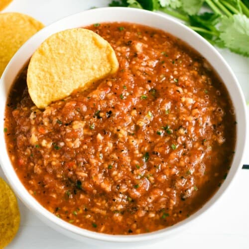 close-up overhead of salsa in a white bowl with a tortilla chip in it.