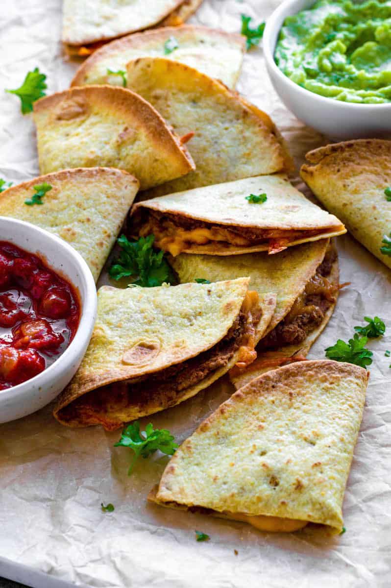 Air fryer quesadillas cut into triangles, and served on a plate layered with parchment paper.