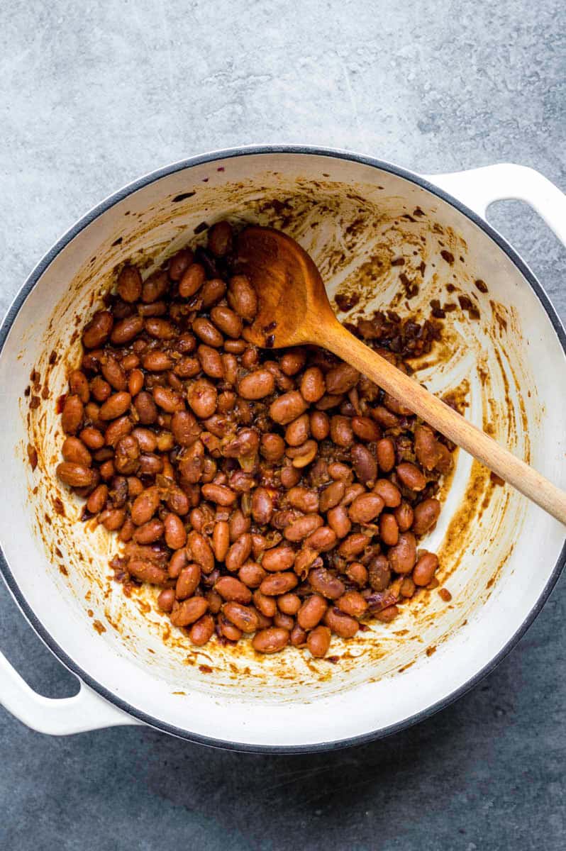 Cooking pinto beans with spices in a white Dutch oven.