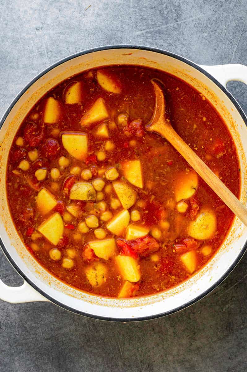 A white dutch oven filled with tomatoes, chickpeas, and potatoes before cooking.