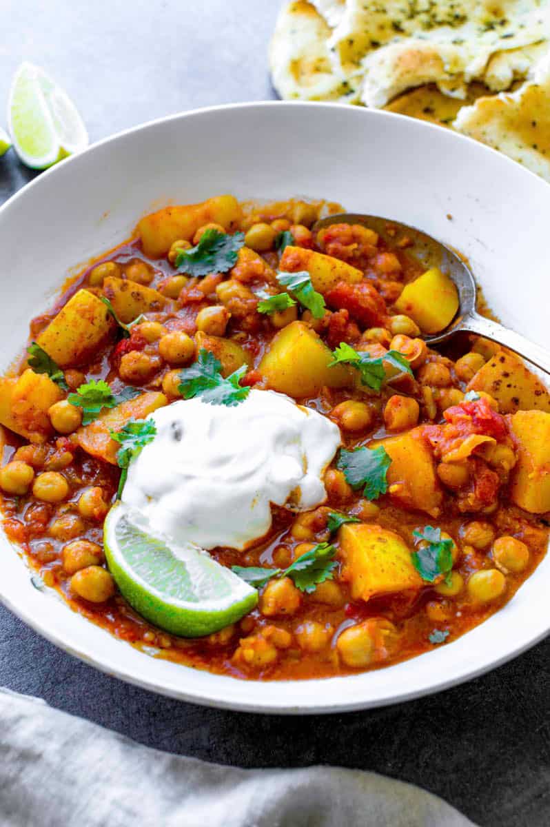 Chickpea and potato curry served in a white bowl and topped with cilantro and a dollap of vegan sour cream.
