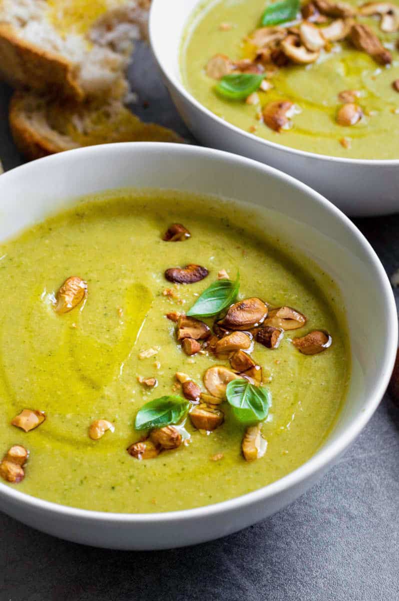 A white bowl filled with vegan broccoli soup and topped with crushed cashews and basil.