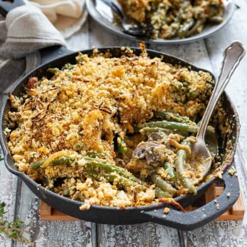 Green bean casserole in a cast iron skillet with serving spoon.