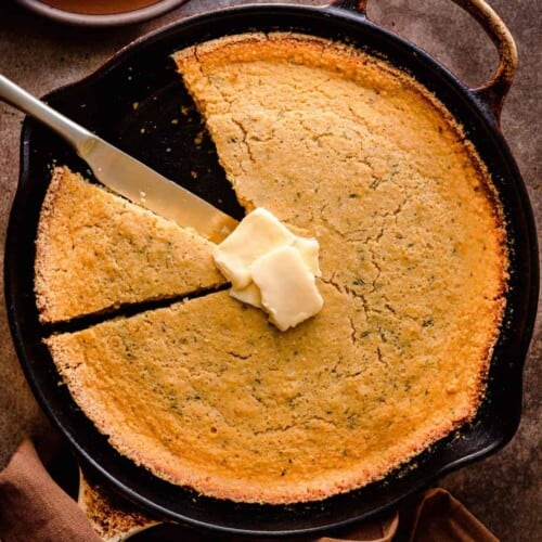 Cornbread in a cast iron skillet topped with pats of vegan butter.