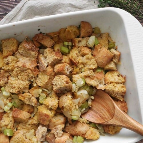 Bread stuffing in a white casserole dish with a wooden spoon.