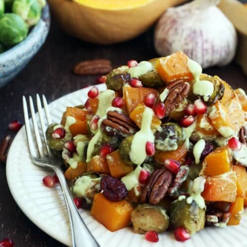 Brussels sprouts and squash on a plate with pecans and pomegranate seeds.