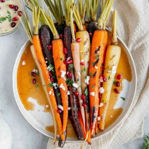 Rainbow colored carrots with green ends on a plate with sauce.