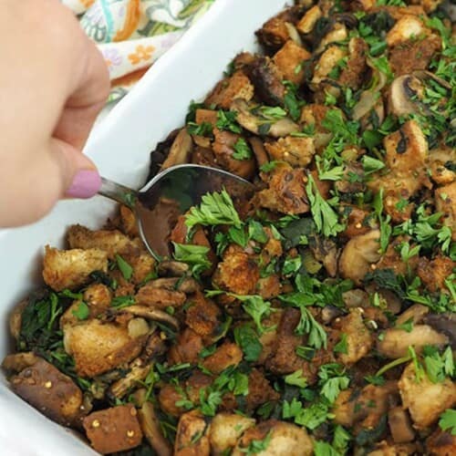 Mushrooms and spinach in rectangle casserole dish with a hand dipping a spoon into it.