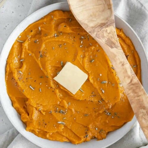 Creamy sweet potatoes in a white serving dish with a spoon propped over the edge.